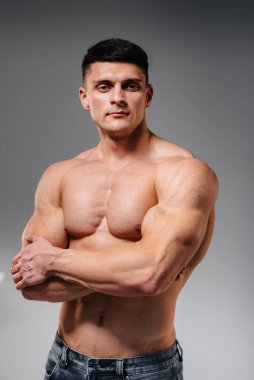 Mükemmel karın kasları olan genç seksi bir sporcu arka planda kot pantolonla stüdyoda üstsüz poz veriyor. Sağlıklı yaşam tarzı, düzgün beslenme, eğitim programları ve kilo vermek için beslenme.