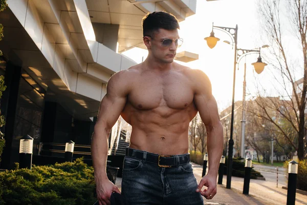 A young sexy athlete with perfect abs poses on the street during the sunset. Healthy lifestyle, proper nutrition, training programs and nutrition for weight loss.