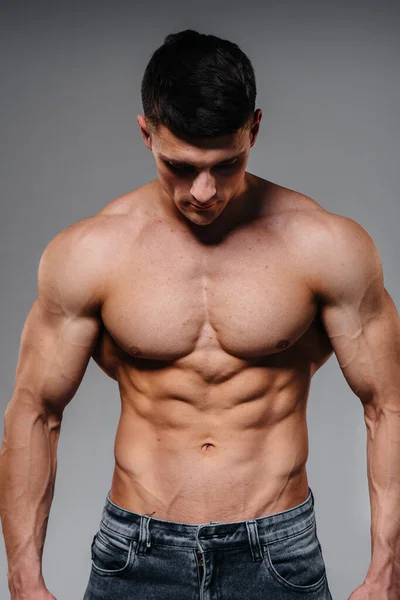 Mükemmel karın kasları olan genç seksi bir sporcu arka planda kot pantolonla stüdyoda üstsüz poz veriyor. Sağlıklı yaşam tarzı, düzgün beslenme, eğitim programları ve kilo vermek için beslenme.
