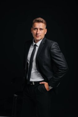 Siyah takım elbiseli ve siyah arka planda gülümseyen yakışıklı bir genç. Temizlen, hazırlan..