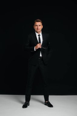 Siyah takım elbiseli yakışıklı bir genç siyah arka planda poz veriyor. Şık bir iş adamı. Büyük bir iş adamı..