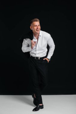 Yakışıklı genç bir adam ceketini çıkarıp siyah arka planda poz vererek gülüyor. Şık bir iş adamı. Büyük bir iş adamı..