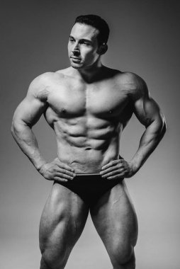 Genç bir sporcu stüdyoda üstsüz poz veriyor, kaslarını ve kaslarını gösteriyor. Siyah ve beyaz.