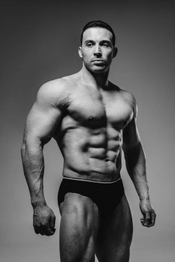 Genç bir sporcu stüdyoda üstsüz poz veriyor, kaslarını ve kaslarını gösteriyor. Siyah ve beyaz.
