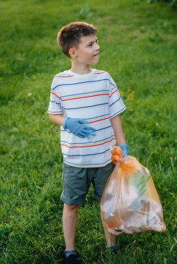 Gün batımında yedi yaşında bir çocuk parkta çöp toplamakla meşgul. Çevre bakımı, geri dönüşüm.