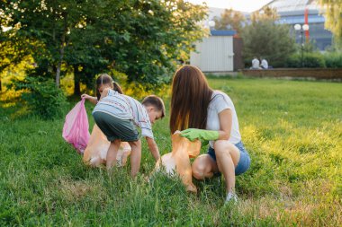 Gün batımında çocuklu bir grup kız parkta çöp toplamakla meşgul. Çevre bakımı, geri dönüşüm.