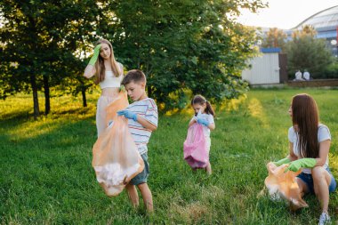Gün batımında çocuklu bir grup kız parkta çöp toplamakla meşgul. Çevre bakımı, geri dönüşüm.