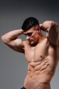 Mükemmel karın kasları olan genç seksi bir sporcu arka planda kot pantolonla stüdyoda üstsüz poz veriyor. Sağlıklı yaşam tarzı, düzgün beslenme, eğitim programları ve kilo vermek için beslenme.