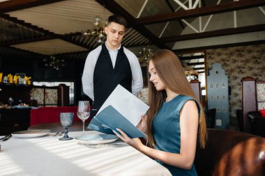 Güzel bir restoranda genç ve güzel bir kadın menüye bakar ve şık önlüklü genç bir garsona sipariş verir. Müşteri hizmetleri.