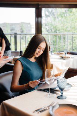 Güzel bir restoranda genç ve güzel bir kadın menüye bakar ve şık önlüklü genç bir garsona sipariş verir. Müşteri hizmetleri.
