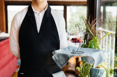 Şık bir üniforma içindeki genç bir garson, güzel bir restoranın yakın çekiminde masanın yanındaki tepside nefis bir tabakla duruyor. Restoran faaliyetleri, en üst düzeyde..
