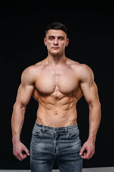 Mükemmel karın kasları olan genç seksi bir sporcu arka planda kot pantolonla stüdyoda üstsüz poz veriyor. Sağlıklı yaşam tarzı, düzgün beslenme, eğitim programları ve kilo vermek için beslenme.