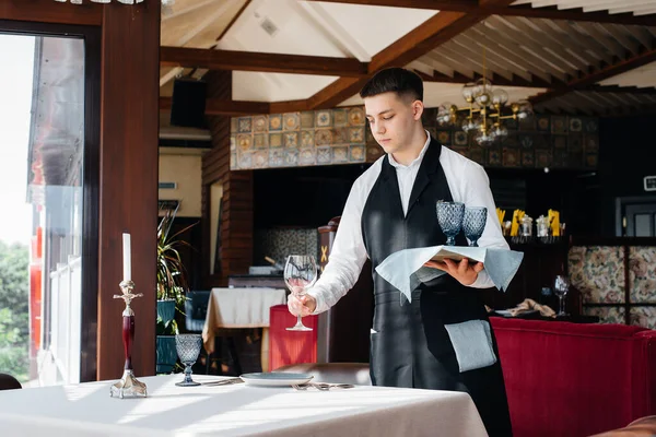 スタイリッシュな制服を着た若い男性ウエイターが美しいグルメレストランでテーブルを提供しています 最高レベルのレストラン活動 — ストック写真