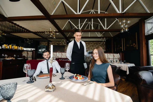 一个时髦的侍者招待一对年轻夫妇 这对年轻夫妇是在一家美食家餐厅里约会的 饮食业的客户服务 — 图库照片