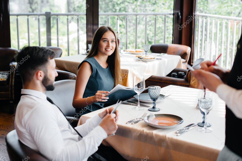 A stylish waiter serves a young couple who came on a date in a gourmet restaurant. Customer service in the catering.