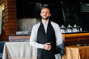 Sakallı genç bir garson önlüğünü giyer ve güzel bir restoranda çalışmaya hazırlanır..