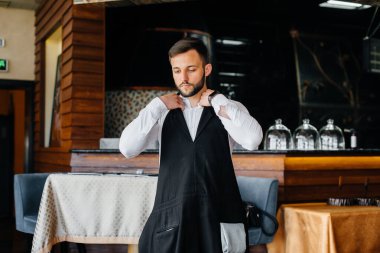 Sakallı genç bir garson önlüğünü giyer ve güzel bir restoranda çalışmaya hazırlanır..