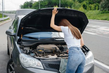 Genç bir kız otoyolun ortasında bozuk bir arabanın yanında duruyor ve kaputun altına bakıyor. Aracın bozulması ve arızası. Yardım bekliyorum..