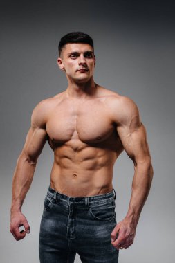 Mükemmel karın kasları olan genç seksi bir sporcu arka planda kot pantolonla stüdyoda üstsüz poz veriyor. Sağlıklı yaşam tarzı, düzgün beslenme, eğitim programları ve kilo vermek için beslenme.