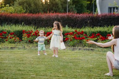 Genç ve güzel bir anne kızıyla birlikte gün batımında çimlerin üzerindeki parkta ilk adımları atmasına yardım eder ve öğretir..