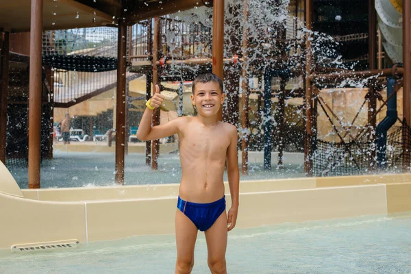 Szczęśliwy Siedmiolatek Uśmiecha Się Pokazuje Klasę Tle Zjeżdżalni Parku Wodnym — Zdjęcie stockowe