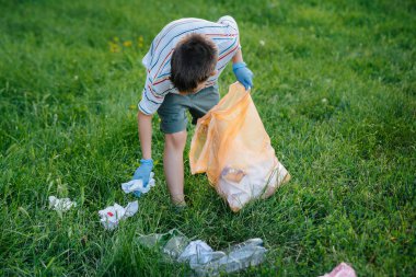 Gün batımında yedi yaşında bir çocuk parkta çöp toplamakla meşgul. Çevre bakımı, geri dönüşüm.