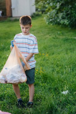 Gün batımında yedi yaşında bir çocuk parkta çöp toplamakla meşgul. Çevre bakımı, geri dönüşüm.