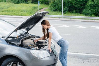 Genç bir kız otoyolun ortasında bozuk bir arabanın yanında duruyor ve kaputun altına bakıyor. Aracın bozulması ve arızası. Yardım bekliyorum..