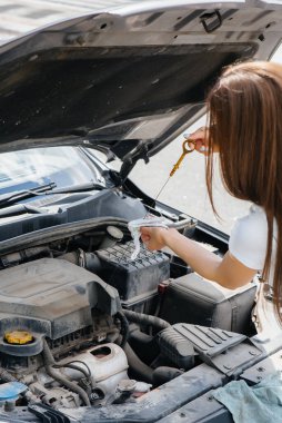 Genç bir kız otoyolun ortasında bozuk bir arabanın yanında duruyor ve motorun yağ seviyesini kontrol ediyor. Aracın bozulması ve arızası. Yardım bekliyorum..