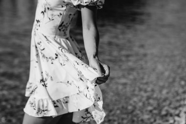 Şapkalı ve açık renk elbiseli güzel bir kadın güneşli bir günde okyanus kıyısında büyük kayaların arkasında yürüyor. Turizm ve tatil gezisi.