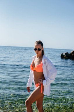 Bikinili güzel bir kadın güneşli bir günde okyanus kıyısında büyük kayaların arkasında yürüyor. Turizm ve turizm gezileri.