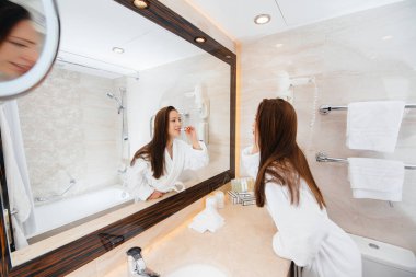 Genç ve güzel bir kız beyaz bir banyoda dişlerini fırçalıyor. Otelde taze günaydın..