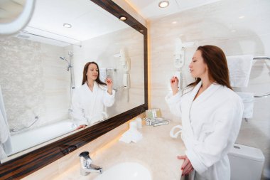 Genç ve güzel bir kız beyaz bir banyoda dişlerini fırçalıyor. Otelde taze günaydın..