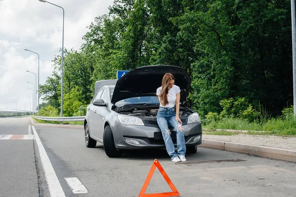 一个年轻的女孩站在高速公路中央一辆抛锚的汽车旁边 打电话求助 汽车故障和抛锚 等人帮忙 — 图库照片