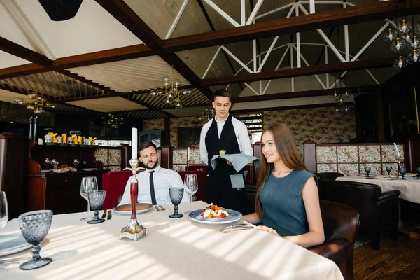 一个时髦的侍者招待一对年轻夫妇 这对年轻夫妇是在一家美食家餐厅里约会的 饮食业的客户服务 — 图库照片