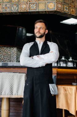 Sakallı genç bir garson önlüğünü giyer ve güzel bir restoranda çalışmaya hazırlanır..