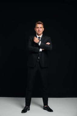 Siyah takım elbiseli yakışıklı bir genç siyah arka planda poz veriyor. Şık bir iş adamı. Büyük bir iş adamı..