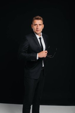 Siyah takım elbiseli yakışıklı bir genç siyah arka planda poz veriyor. Şık bir iş adamı. Büyük bir iş adamı..