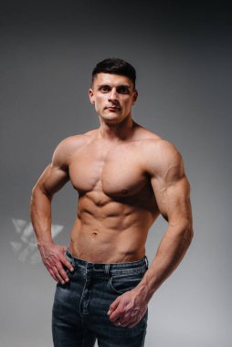 Mükemmel karın kasları olan genç seksi bir sporcu arka planda kot pantolonla stüdyoda üstsüz poz veriyor. Sağlıklı yaşam tarzı, düzgün beslenme, eğitim programları ve kilo vermek için beslenme.