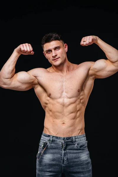 Mükemmel karın kasları olan genç seksi bir sporcu arka planda kot pantolonla stüdyoda üstsüz poz veriyor. Sağlıklı yaşam tarzı, düzgün beslenme, eğitim programları ve kilo vermek için beslenme.