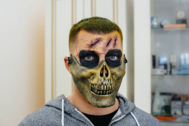 Cadılar Bayramı tatili için stüdyoda, kafatası şeklinde güzel, ürkütücü makyajlı genç bir adam. Mutlu Cadılar Bayramı konsepti.