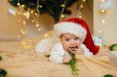 Sevimli gülümseyen bebek, Noel ağacının altında yatıyor ve hediyelerle oynuyor. Noel ve Yeni Yıl kutlamaları