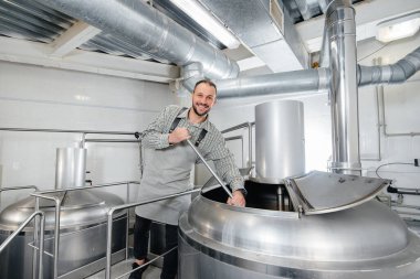 Genç bir erkek bira imalatçısı küçük bir bira fabrikasında demleme işlemiyle meşgul. Bira üretimi.