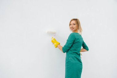 Genç bir kız silindirle beyaz bir duvar boyuyor. İç kısmın tamiri.