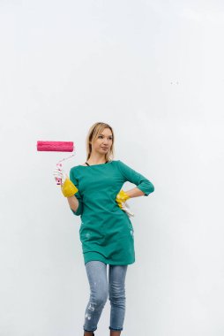 Genç bir kız beyaz bir duvar boyamadan önce pembe bir silindirle poz veriyor. İç kısmın tamiri.