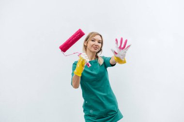 Genç bir kız beyaz bir duvar boyamadan önce pembe bir silindirle poz veriyor. İç kısmın tamiri.