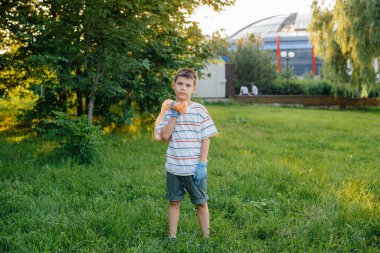 Gün batımında yedi yaşında bir çocuk parkta çöp toplamakla meşgul. Çevre bakımı, geri dönüşüm.