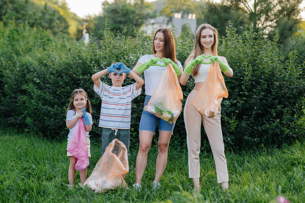 A group of young women with children show hearts after cleaning garbage in the park during sunset. Environmental care, recycling.