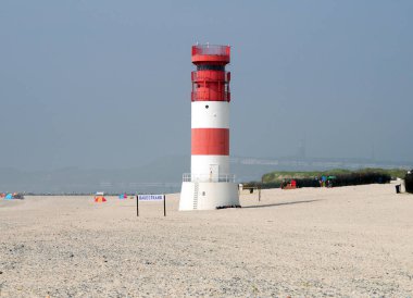 Picturesque Red White Lighthouse On The Beach Of The North Sea Island Helgoland On A Hazy And Sunny Summer Day With A Clear Blue Sky clipart