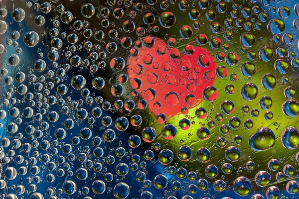 Multi colored drops of water are located on a blue-green background with a red silhouette of the heart. Abstract fantasy. 3D render.